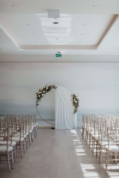 an empty room with rows of chairs and white drapes on the wall, decorated with flowers