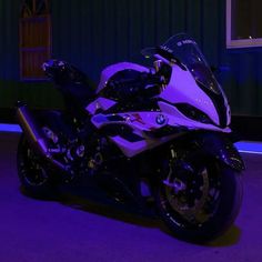 a purple motorcycle parked in front of a green building with blue lights on it's side