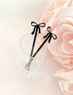 two black scissors sticking out of a glass vase with pink flowers in the back ground