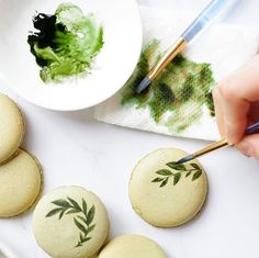 someone is painting leaves on some cookies with green icing and paintbrushes next to them