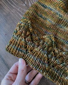 a hand holding a knitted hat on top of a wooden table next to a person's finger