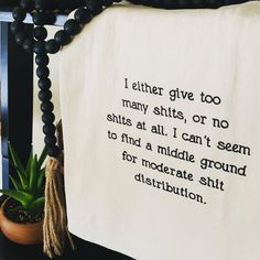 a white tea towel with black writing on it next to a potted plant and beaded necklace