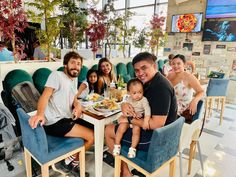 a group of people sitting at a table with food in front of them and smiling for the camera