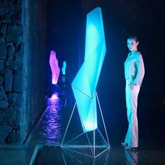 a man standing next to a sculpture in a dark room with blue light coming from it