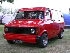 a red van parked on top of a grass covered field