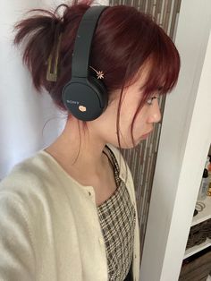 a woman with red hair wearing headphones in front of a door and looking into the distance