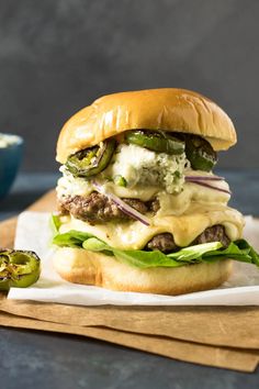 a cheeseburger with pickles and onions on a cutting board next to a bowl of ranch dressing