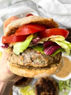 a hamburger with lettuce, tomato and other toppings is being held up by someone's hand