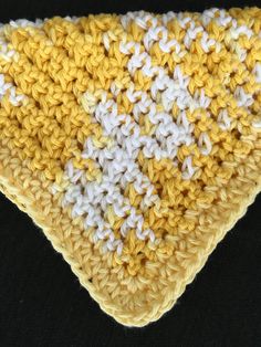 a yellow and white crocheted triangle on a black surface