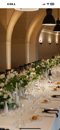 the long table is set with white flowers and place settings for an elegant dinner party