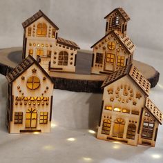 small wooden houses with lights on them sitting on a table next to a slice of wood