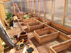 the inside of a greenhouse with wooden planters and tools on the ground next to it