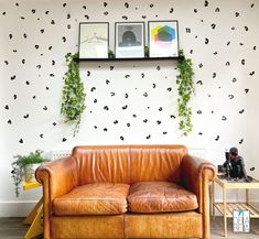 a brown leather couch sitting in front of a wall with pictures on it and plants