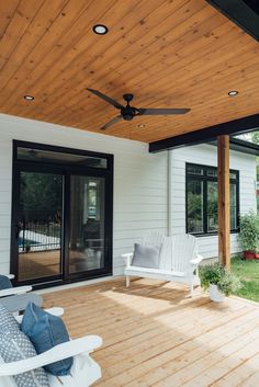 a porch with two white chairs and a ceiling fan on the side of the house