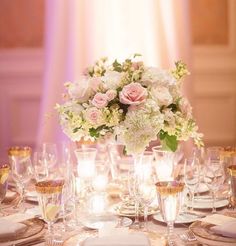 the centerpieces on this table are filled with white and pink flowers, which is accented with gold rimmed glassware