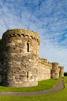 an old stone castle sitting on top of a lush green field under a blue sky