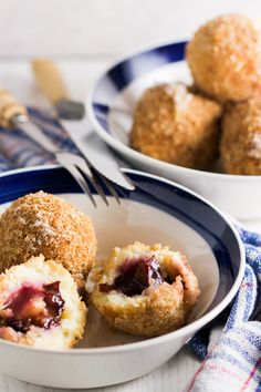 two plates with pastries on them next to a fork and bowl full of fruit