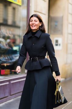 a woman is walking down the street with her hand in her pocket and wearing a black coat