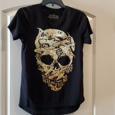 a black t - shirt with a gold skull on it hanging from a white door