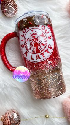 a starbucks cup with glitter on it sitting on a white fur covered floor next to christmas ornaments