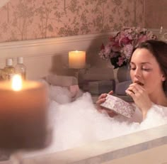 a woman sitting in a bathtub with candles on the side and her mouth open