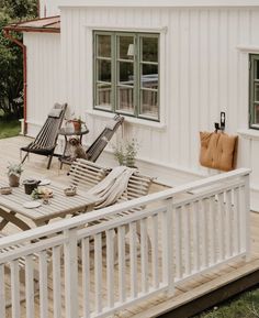 a deck with chairs and tables on it next to a white house in the background