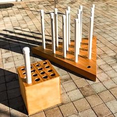 a wooden structure with white poles and holes in the middle on a brick walkway next to a parking lot