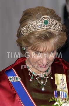 a woman wearing a tiara and holding a bouquet in front of her face with other people looking on