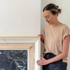 a woman standing in front of a painting holding the frame with her hands and looking at it