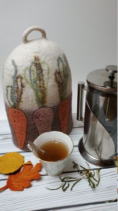 a tea pot next to a cup with leaves on it