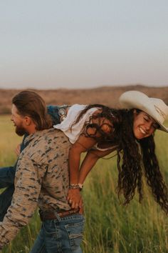 a man carrying a woman on his back in the middle of an open field with tall grass