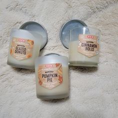 three candles sitting next to each other on top of a white blanket with the label pumpkin pie