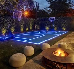 an outdoor basketball court is lit up at night with blue lights and fire pit in the foreground