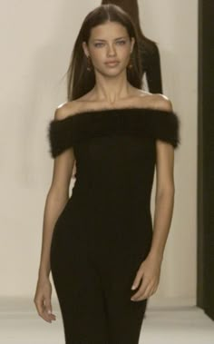 a model walks down the runway in a black dress with fur trims on her shoulders