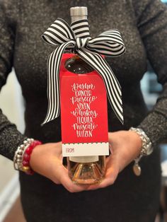 a woman holding a bottle of wine with a ribbon around it's neck and label