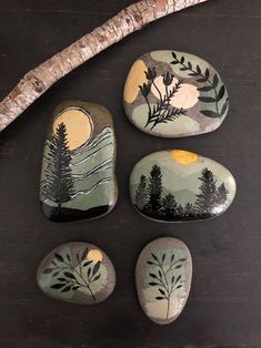 four painted rocks sitting on top of a wooden table next to a stick and twig