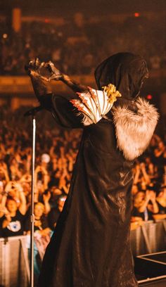 a woman dressed in black performing on stage with an audience behind her at a concert