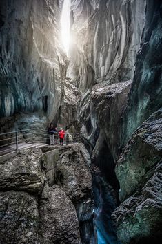 two people are standing in the middle of a narrow canyon with water running through it