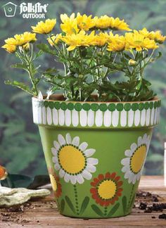 yellow flowers in a green flower pot on a wooden table with an orange and white planter