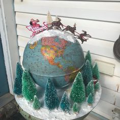 a globe with christmas trees and santa clause on top is sitting in front of a house