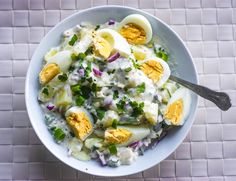 a bowl filled with eggs and vegetables on top of a white tile floor next to a spoon