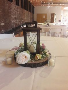 a candle and some flowers on a table in a room with white tables cloths