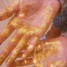 two hands covered in gold glitter with their fingers spread out to show the sparkle on them