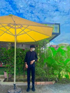 a man wearing a face mask standing under an umbrella in front of some plants and trees