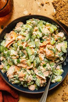 a bowl filled with chicken salad next to bread and a glass of wine on the side