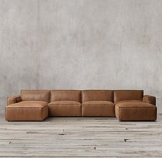 a brown leather couch sitting on top of a wooden floor next to a cement wall