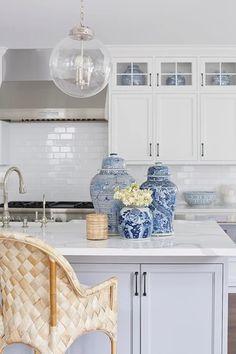 a white kitchen with blue and white vases on the counter top, two chairs in front of an island