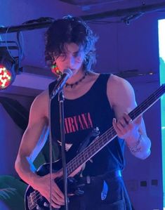 a man holding a guitar while standing in front of a microphone and wearing a tank top