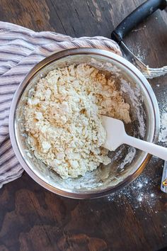 a wooden table with a metal mixing bowl filled with flour and a white spatula