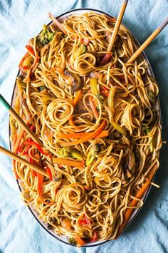 a plate full of noodles and vegetables with chopsticks